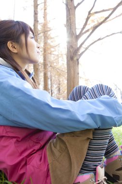 Sarı sırt çantalı genç Japon kadın sonbahar parkında yürüyüş yapıyor.