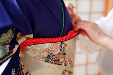 Kadın elleri, geleneksel Japon kimonosu giyen bir kadına yardım eder. 