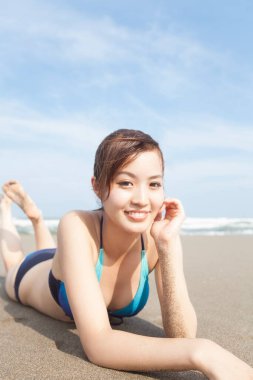 Genç Asyalı kadın yaz kumsalında kumların üzerinde yatıyor.