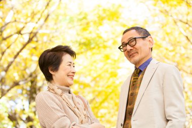 Parkta gülümseyen yüzleriyle yürüyen yaşlı bir çift.