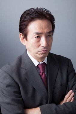 Gri arka planda orta yaşlı Japon işadamı. Gri takım elbiseli Asyalı adamın portresi. 