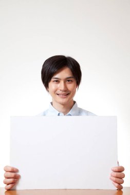 Genç Asyalı adam, elinde beyaz boşluk tutuyor.