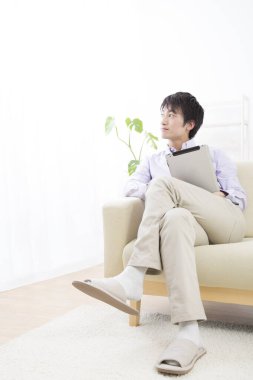 Kanepede tabletli Asyalı adam. 