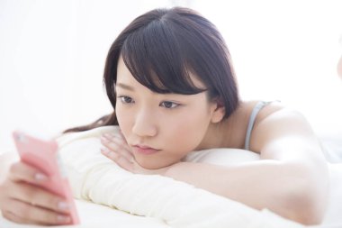 Akıllı telefondan Asyalı genç bir kadın bakıyor.