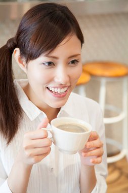 Kafede elinde fincan tutan Asyalı kadının portresi. 