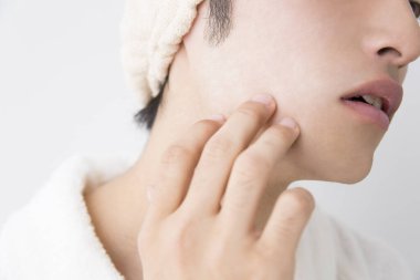 Genç adam beyaz arka planda tenine dokunuyor, yakın plan.