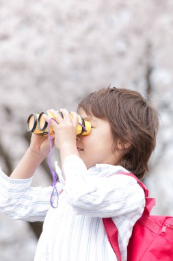 Dürbünü olan çocuk çiçek açan ağaçlarla parkta. 