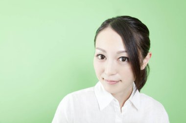 Beyaz gömlekli genç bir kadın yeşil arka planda izole edilmiş kameraya bakıyor. 