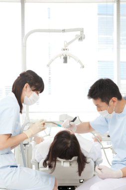 Asyalı erkek ve kadın dişçiler hastanın ağzını inceliyor.