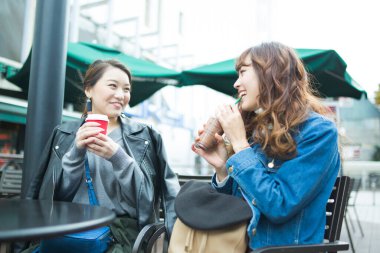 İki Asyalı genç arkadaş sokakta kahve içerek eğleniyorlar. 