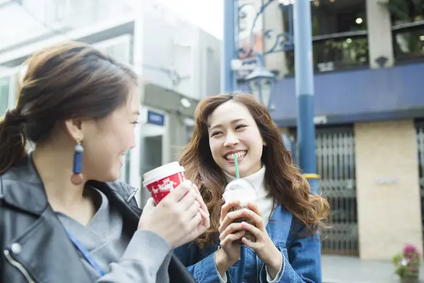 two young asian friends having fun together drinking coffee on street