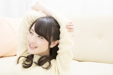 Genç Asyalı kadın kanepede dinleniyor.