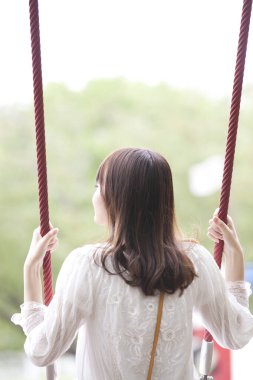 Genç bir kadın parkta salıncakta oturuyor.