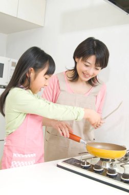 Gülümseyen Japon kadın ve kızı mutfakta yemek pişiriyor.