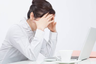 Yorgun, başı ağrıyan Asyalı iş kadını laptopuyla masada oturuyor ve ofisinde çalışıyor..