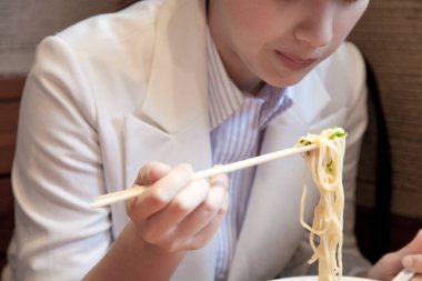 Mutfakta çubuklarla erişte yiyen bir kadın.