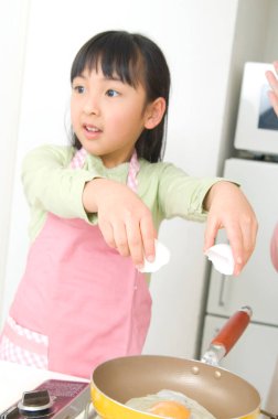 Küçük Asyalı kız annesiyle mutfakta kızarmış yumurta pişiriyor. 