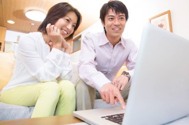 Genç Asyalı çift evdeki oturma odasında dizüstü bilgisayar kullanıyor.