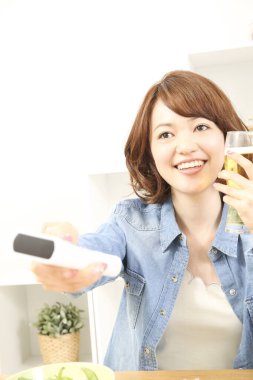 Neşeli Japon kadın televizyon izlerken bira içiyor. Uzaktan kumanda elinde