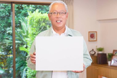 Üst düzey Asyalı adam oturma odasında beyaz tabela gösteriyor.