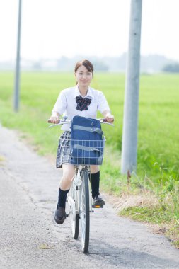 Kırsalda bisiklet süren gülümseyen Asyalı kız.