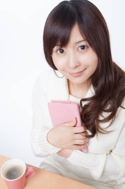 Masasında kitap ve kahve olan genç bir kadın. 