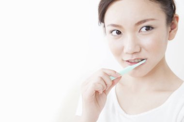 Genç Asyalı kadın dişlerini fırçalıyor.