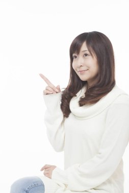 Süveter giyen Asyalı kadın beyaz arka planı işaret ediyor.