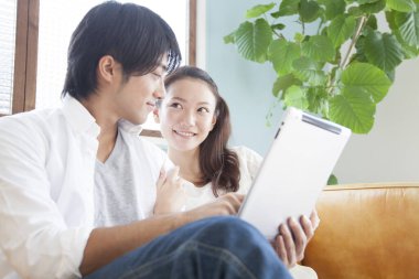 Mutlu Asyalı adam oturma odasında rahatlamak için tablet bilgisayar kullanıyor.