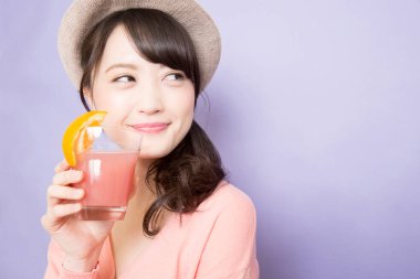 Bir bardak taze meyve suyuyla şapkalı güzel Asyalı kadının stüdyo fotoğrafı.