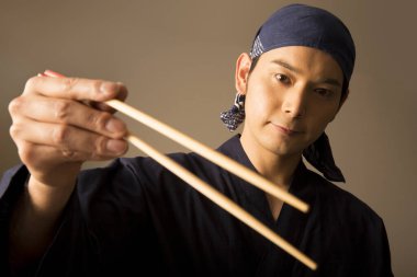 Şef elinde yemek çubukları tutuyor. 