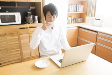 Evde dizüstü bilgisayar kullanan kahve fincanı olan genç bir adam. 