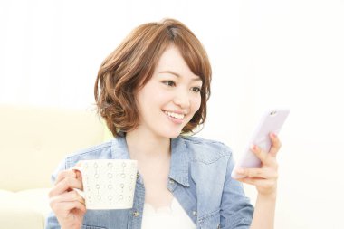 Elinde fincanla evde telefon kullanan güzel bir Japon kadının portresi.