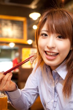 Restoranda yemek çubuklarıyla yemek yiyen Asyalı kadın. 