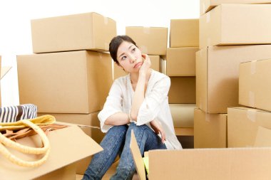 Yeni evinde karton kutularla oturan düşünceli genç bir kadın. 