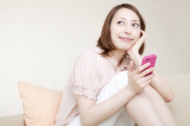 Kanepede oturan ve akıllı telefon kullanan genç bir kadın.