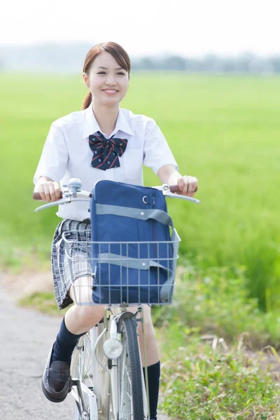 stock image smiling Asian schoolgirl riding bicycle in countryside