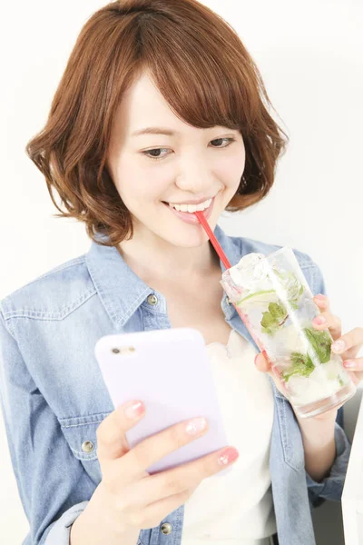 Genç Japon kadın limonlu ferahlatıcı su içerken elinde akıllı telefon tutuyor.