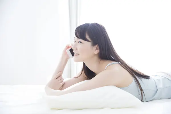 asian woman talking on smartphone on bed