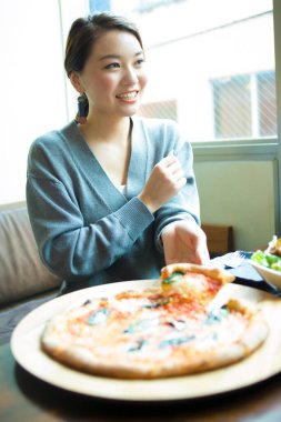 Kafede pizza yiyen Asyalı bir kadının portresi.