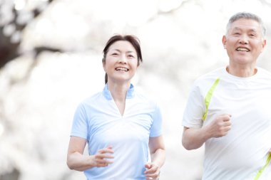 Parkta çiçek açan ağaçlarla koşan Asyalı olgun bir çift.