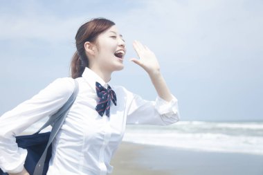 Okul üniformalı güzel Japon kız sahilde çığlık atarak eğleniyor.
