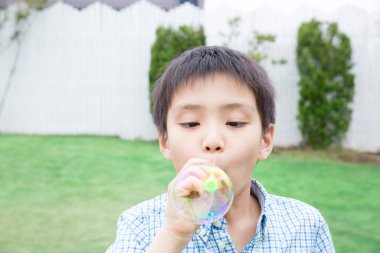 Çocuk bahçede balon üflüyor.