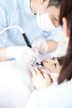 Asyalı erkek ve kadın dişçiler hastanın ağzını inceliyor.