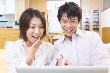 Genç mutlu Japon çift odada dizüstü bilgisayar kullanıyor.