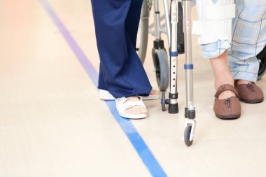 Hemşire adama hastanede yürümesi için yardım ediyor.