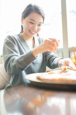 Kafede pizza yiyen mutlu Asyalı kadın.