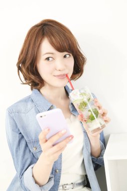 Genç Japon kadın limonlu ferahlatıcı su içerken elinde akıllı telefon tutuyor.