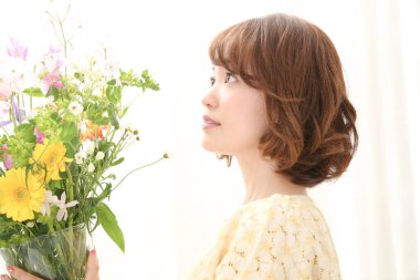 Bir buket taze çiçekle gülümseyen genç Japon kadın.