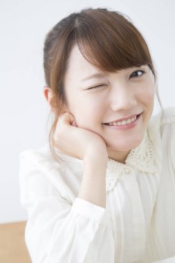 Genç Asyalı kadın gülümsüyor ve göz kırpıyor. 